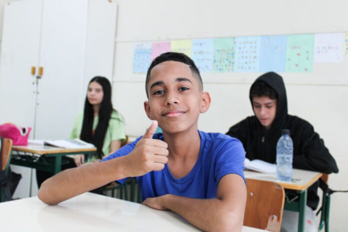 Estudantes e professor conversam em roda durante atividade em sala de aula de escola estadual
